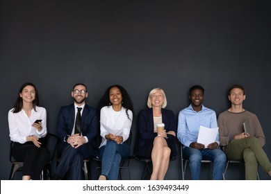 Near black wall studio background sitting six diverse happy entrepreneurs, successful corporate staff members, businesspeople ready for negotiation, wait for job interview sit in row queue, hr concept - Powered by Shutterstock