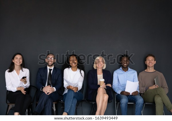 Near black wall studio background sitting six\
diverse happy entrepreneurs, successful corporate staff members,\
businesspeople ready for negotiation, wait for job interview sit in\
row queue, hr concept