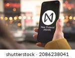 Near Protocol cryptocurrency symbol, logo. Business and financial concept. Hand with smartphone, screen with crypto icon close-up