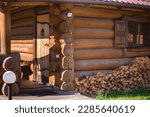 A neat large woodpile against the background of a wooden house made of logs with a small window. Sunny spring or summer day