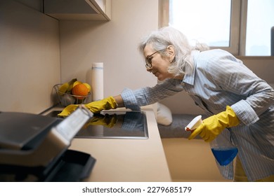 Neat pensioner washes the kitchen stove with a soft cloth