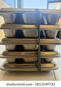 A neat stack of durable stainless steel or aluminum baking pans, molds, or food containers, securely tied with a plastic rope. Ready for commercial kitchen use, catering, or baking business