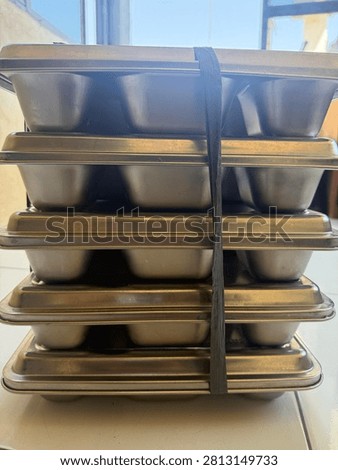 A neat stack of durable stainless steel or aluminum baking pans, molds, or food containers, securely tied with a plastic rope. Ready for commercial kitchen use, catering, or baking business