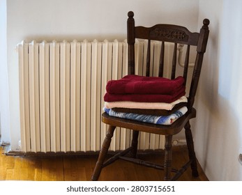 A neat stack of folded colorful bath towels resting on a vintage wooden chair next to a white heating radiator in a cozy room.