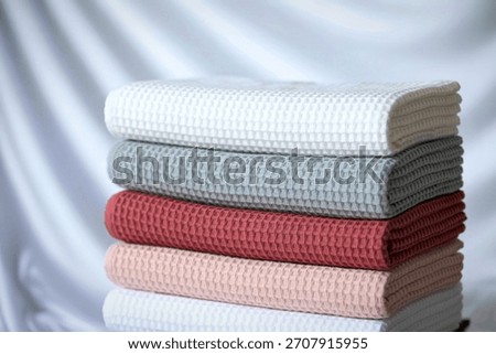 A neat stack of four textured knit blankets in soft pastel shades, presented against a draped white background.