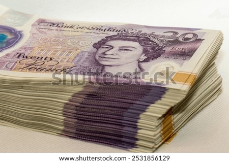 A neat stack of twenty pound banknotes from the Bank of England, featuring a portrait of Queen Elizabeth II, with the denomination Twenty Pounds printed prominently.