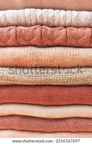 Neat stack of woolen sweaters in pastel beige, pink and orange tones. Autumn and winter fashion aesthetic. Textured wool background.