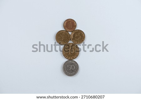 A neat vertical stack of German pfennig coins—1, 5, 10, and 50—against a pale blue background, illustrating money, savings, and everyday finance in a simple, balanced composition.