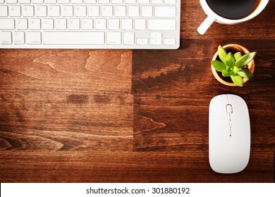 Neat workstation on a wooden desk viewed from overhead with a wireless computer mouse and keyboard, cup of coffee and houseplant