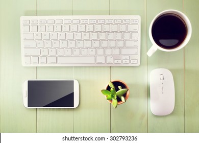 Neat Workstation On A Wooden Desk Viewed From Overhead With A Wireless Computer Mouse And Keyboard, Mobile Phone, Cup Of Coffee And Houseplant