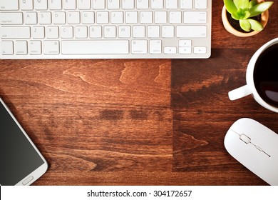 Neat Workstation On A Wooden Desk Viewed From Overhead With A Wireless Computer Mouse And Keyboard, Mobile Phone, Cup Of Coffee And Houseplant