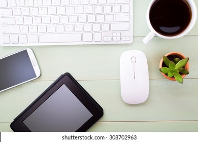 Neat Workstation On A Wooden Desk Viewed From Overhead With A Wireless Computer Mouse And Keyboard, Mobile Phone, Tablet, Cup Of Coffee And Houseplant