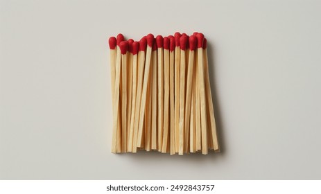 A neatly arranged group of wooden matchsticks with red tips, placed on a light background. The matchsticks are stacked closely together, showcasing their uniformity and vibrant red heads. - Powered by Shutterstock