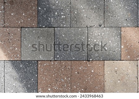 Neatly arranged section of pavement made of rectangular cobblestones. Material exhibiting variety of colors ranging from light beige to dark grey. Sharp edges