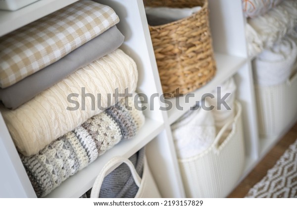 Neatly folded linen cupboard shelves storage\
at eco friendly straw basket placed closet organizer drawer\
divider. Stacks towels pillows plaids soft sheets bedding cabinet\
filling Nordic\
organization