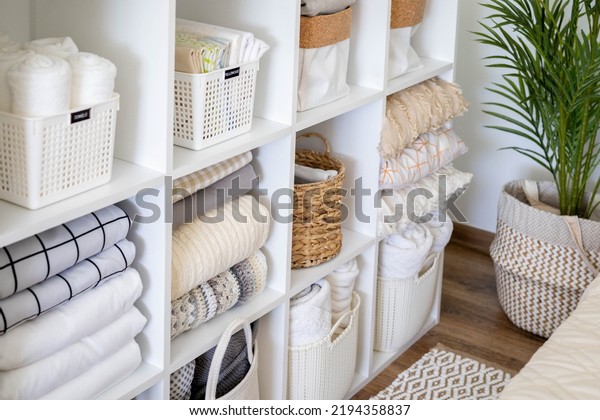 Neatly folded linen cupboard shelves storage\
at eco friendly straw basket placed closet organizer drawer\
divider. Stacks towels pillows plaids soft sheets bedding cabinet\
filling Nordic\
organization