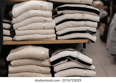 Neatly folded sweaters of various sizes arranged on wooden shelves in a clothing store, showcasing organized retail apparel display. - Powered by Shutterstock - Get 15% off with code: PIKWIZARD15