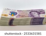 A neatly stacked pile of British twenty pound banknotes, featuring Queen Elizabeth IIs portrait and the Bank of Englands logo. The image captures the details and security features of the currency.