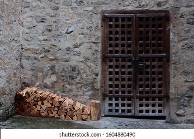 Neatly Stacked Pile of Chopped Fire Wood Logs for Winter Beside Old Metal Portcullis Gate Door with Stone Wall background in a Medieval Castle Chateau in Switzerland