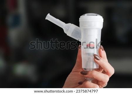 Nebulizator in hand background. Nebulizer isolated. Medical device background. Woman hand holding nebulizator. Lungs and throat treatment. Mouth inhaler.