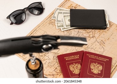 The Neck Of A Bottle Of Red Wine With A Corkscrew In The Cork, A Map Of The World, Two Passports, Money In A Black Wallet And Sunglasses. Selective Focus. Inscription - Passport Russian Federation