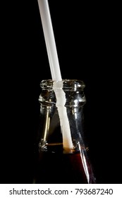 A neck of a cola bottle with a straw close-up on a black background