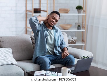 Neck Pain. African American Man Massaging Aching Neck Suffering From Ache Sitting And Working At Laptop On Couch In Living Room At Home. Osteoarthritis, Health Problem Concept.