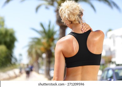 Neck pain during training. Athlete running Caucasian blond woman runner with sport injury in sports bra rubbing and touching upper back muscles outside after exercise workout in summer. - Powered by Shutterstock