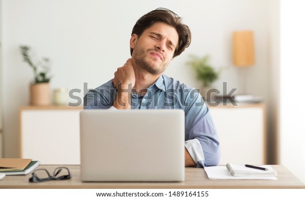 Neck Pain. Man Having Bad Neckache Working On\
Laptop At Workplace.