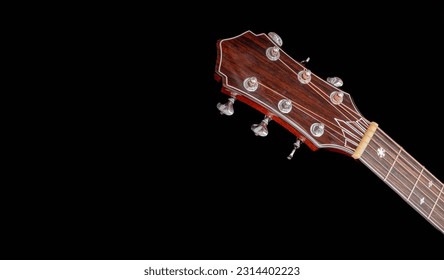 The neck of a six-string acoustic guitar on a dark background . guitar neck on a black background. Wooden neck of a 6-string acoustic guitar. Guitar fingerboard, head stock and tuning machine.