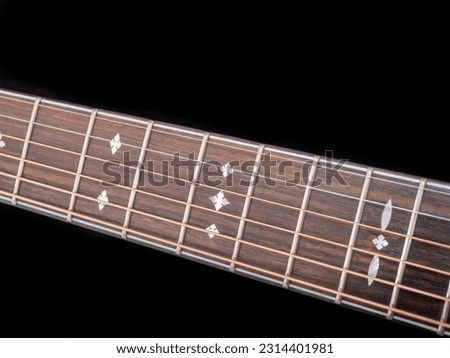 The neck of a six-string acoustic guitar on a dark background . guitar neck on a black background. Wooden neck of a 6-string acoustic guitar. Guitar fingerboard. selective focus.