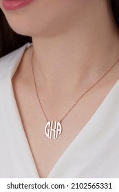 The Necklace With The Initials Of GKA Is Worn Around The Neck Of The Woman Dressed In White. Silver Necklace Image For E-commerce And Online Sales. Personalized Gift Image.