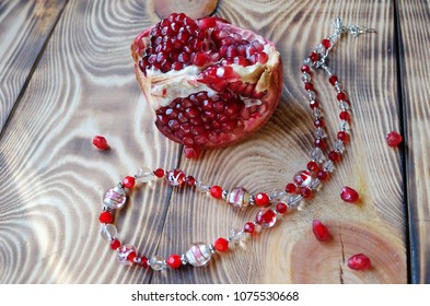 Necklace Of Murano Beads And A Piece Of Ripe Pomegranate On A Wooden Background.