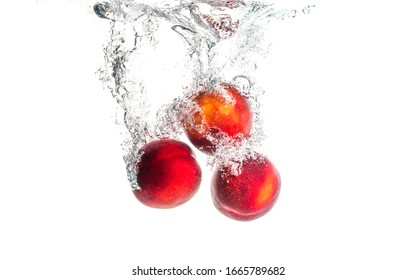 Nectarine fruits splashing into water and sinking with air bubbles isolated on white background. Copy space