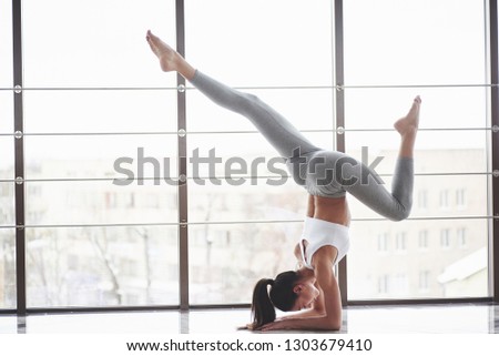Need concentration. Side view of girl in sportswear doing stretch exercises in the big spacious gym.
