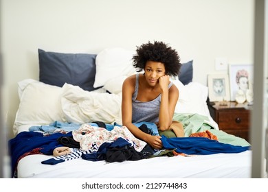 I Need New Clothes. Shot Of An Unhappy Young Woman Getting Dressed With Piles Of Clothing On Her Bed.