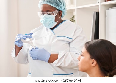 Need A Result. Waist Up Portrait Of The Competent Nurse Being At Her Workplace, While Putting Covid 19 Test At The Protective Place. Woman Patient Sitting At The Cabinet And Looking At The Medical