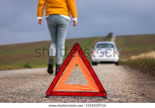 I need roadside\
assistance! Woman and broken car on road. Safety first. Warning\
triangle on road