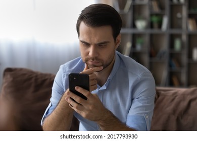 Need To Think. Thoughtful Millennial Man Sit On Couch Rub Chin Read Serious Important Message On Phone Screen. Concentrated Pensive Young Businessman Receive Unexpected News Ponder On Problem Solution