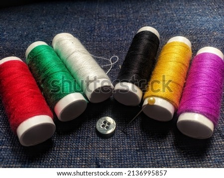 a needle, a black button and six threads with red, green, white, black, yellow and pink colour