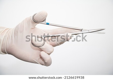 Needle holder in doctor hand with disposable glove on white background. Physician surgeon holds needle forceps or driver. Medical equipment of stainless tool for surgery.