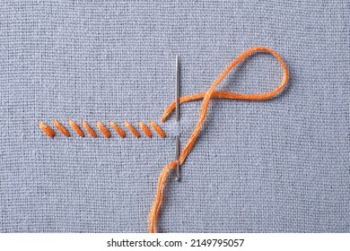 Needle with orange embroidery floss and row of stitches on grey fabric, top view - Shutterstock ID 2149795057