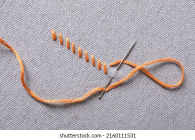 Needle with orange embroidery floss and row of stitches on grey fabric, top view - Shutterstock ID 2160111531
