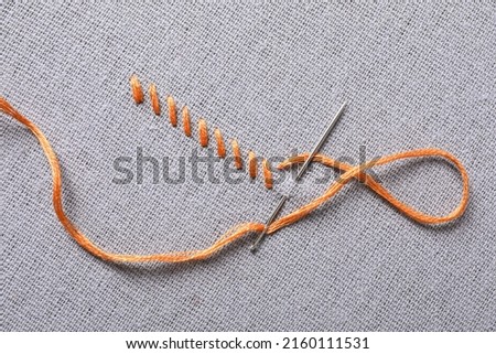 Needle with orange embroidery floss and row of stitches on grey fabric, top view