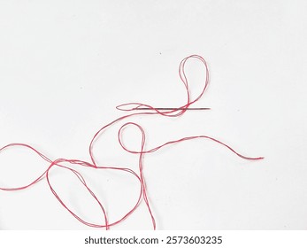 A needle and a piece of red thread are lying on white background 