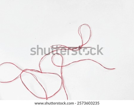 A needle and a piece of red thread are lying on white background 