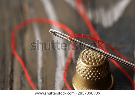 A needle with thread and a thimble on an old wooden table