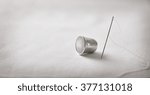 Needle with thread and thimble on white fabric background. Horizontal composition. Front view