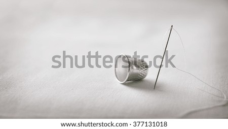 Needle with thread and thimble on white fabric background. Horizontal composition. Front view