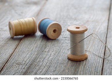 needle and thread and vintage thread spools on wooden background, needlework, design and clothing repair concept